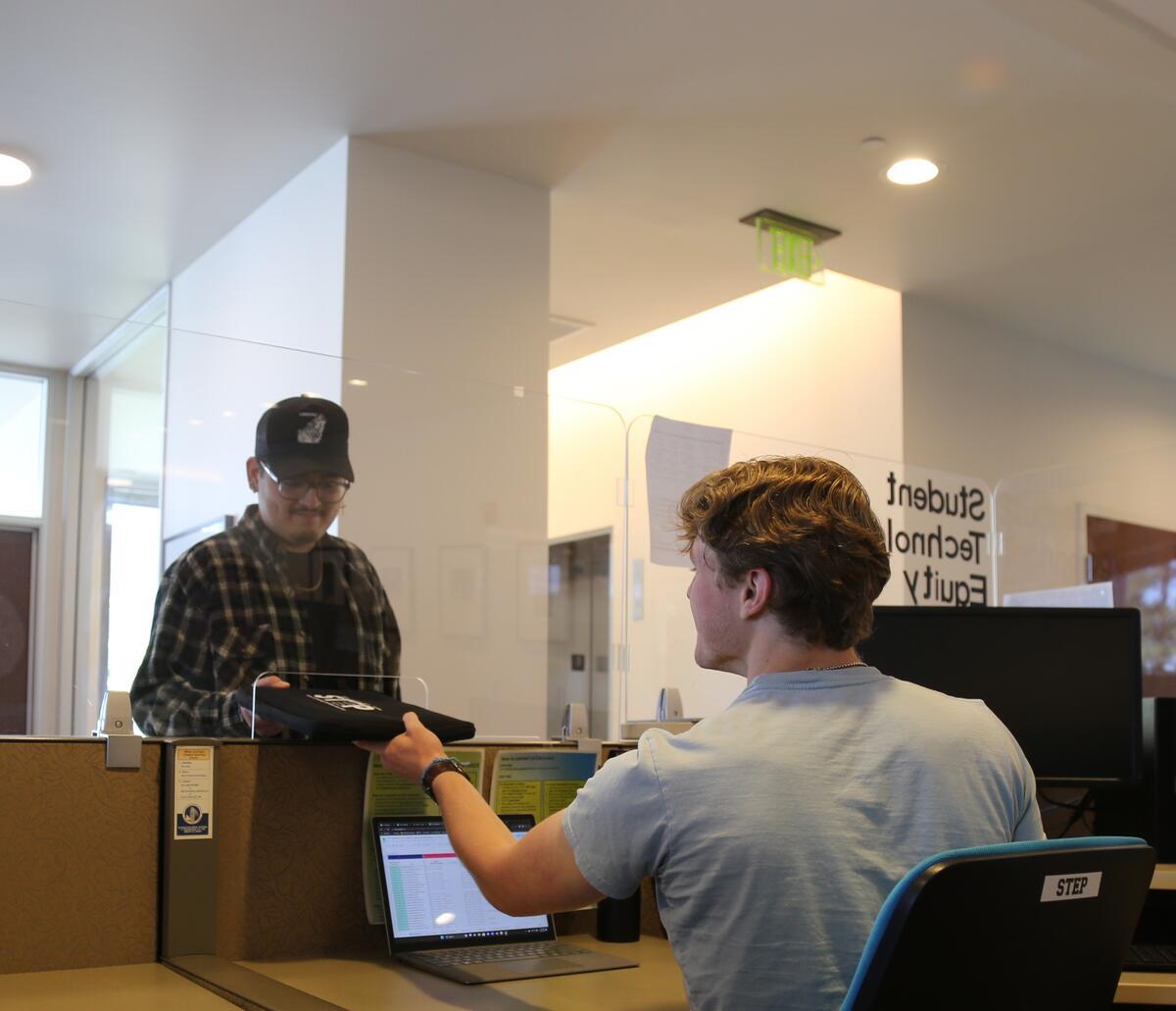 Photo depicts student in glasses and hat collecting their STEP-loaned laptop.